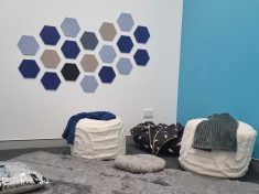 A clinic room with one blue wall and one white wall with blue and grey hexagons. A soft grey carpet and white ottomans with blankets thrown over